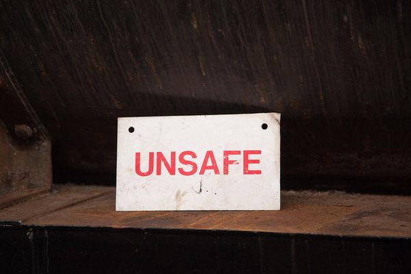 A workshop, with a metal table that looks like it has rust on it.  On the table, a white sign with the word 'unsafe' in red.