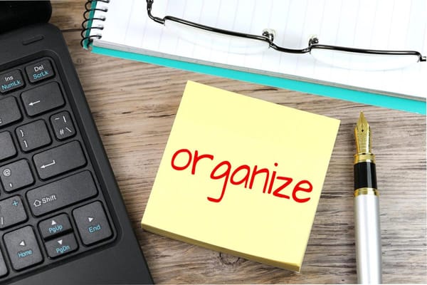 A post-it note with the word "organize".  On the left, a keyboard; to the right, a pen; above, a notebook.